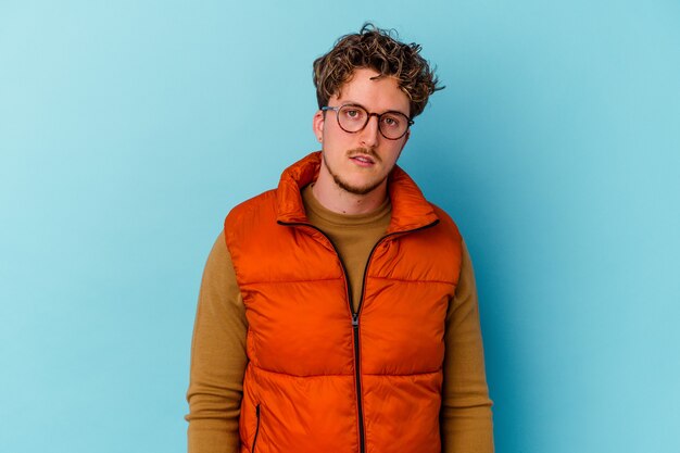 Young caucasian man wearing eyeglasses isolated on blue background sad, serious face, feeling miserable and displeased.