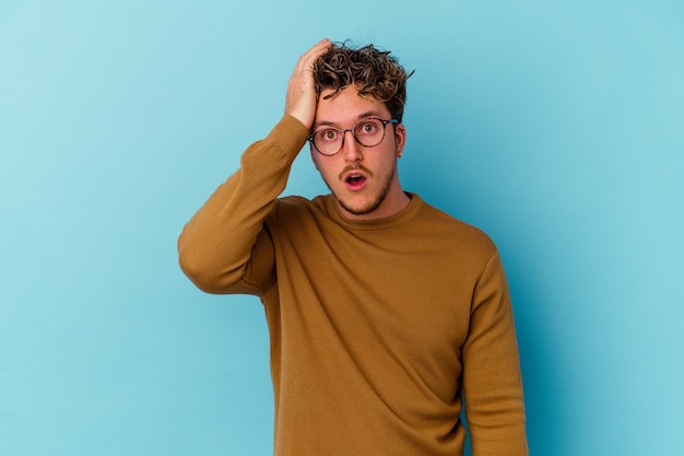 Young caucasian man wearing eyeglasses isolated on blue wall being shocked, she has remembered important meeting.