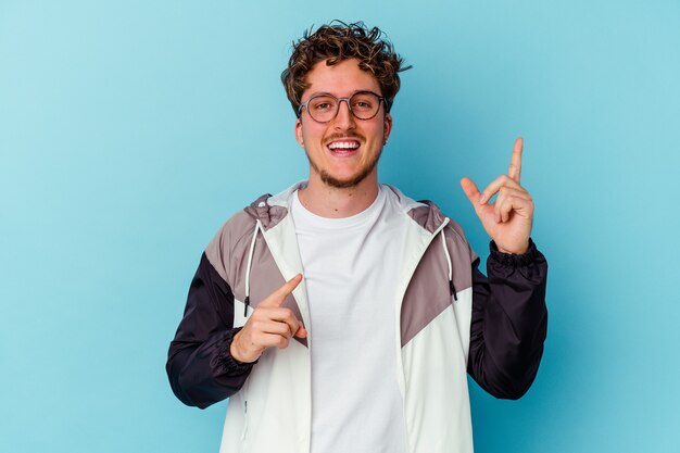 Young caucasian man wearing eyeglasses isolated on blue wall dancing and having fun.