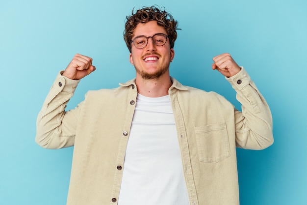 Photo young caucasian man wearing eyeglasses isolated on blue wall showing strength gesture with arms, symbol of feminine power