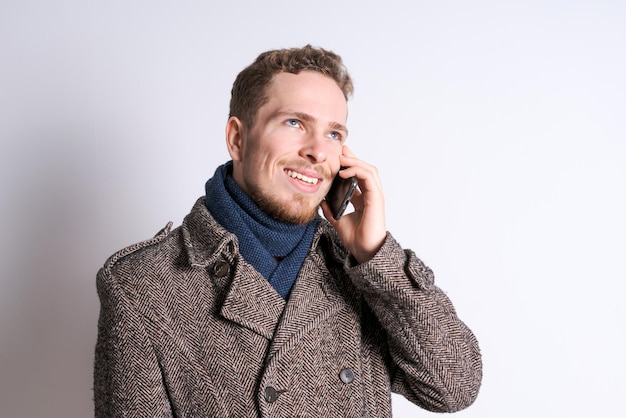 Young caucasian man wearing a fashionable long coat with a scarf standing
