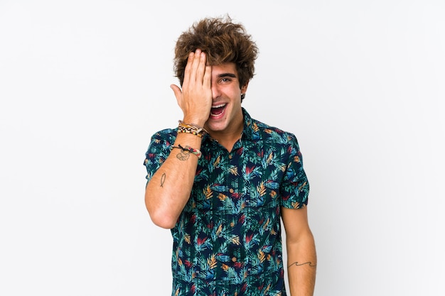 Young caucasian man wearing a flower t-shirt isolated having fun covering half of face with palm.