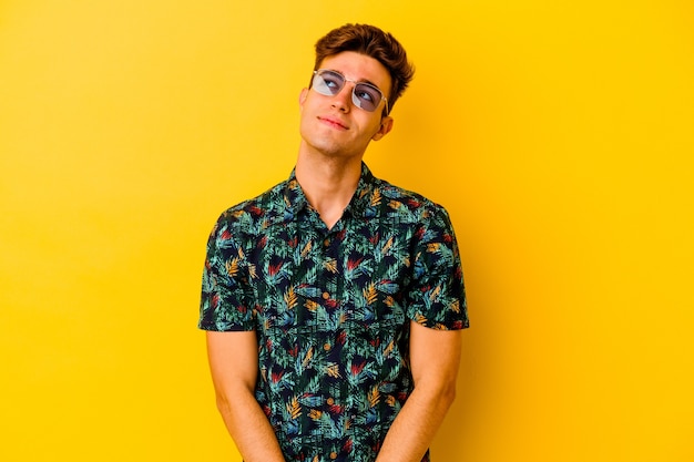 Young caucasian man wearing a Hawaiian shirt isolated on yellow wall dreaming of achieving goals and purposes