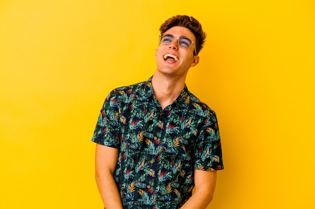 Young caucasian man wearing a Hawaiian shirt isolated on yellow wall relaxed and happy laughing, neck stretched showing teeth