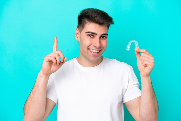 Young caucasian man wearing holding invisible braces isolated on blue background pointing up a great idea