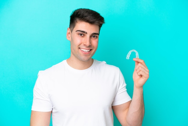 Young caucasian man wearing holding invisible braces isolated on blue background smiling a lot