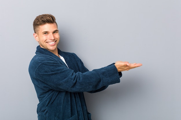 Young caucasian man wearing pajama holding a copy space on a palm.