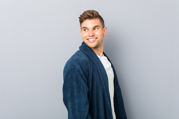 Young caucasian man wearing pajama looks aside smiling, cheerful and pleasant.