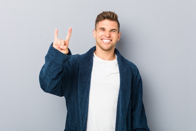 Young caucasian man wearing pajama showing a horns gesture as a revolution concept.