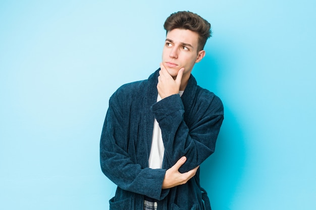 Young caucasian man wearing pajamas looking sideways with doubtful and skeptical expression.