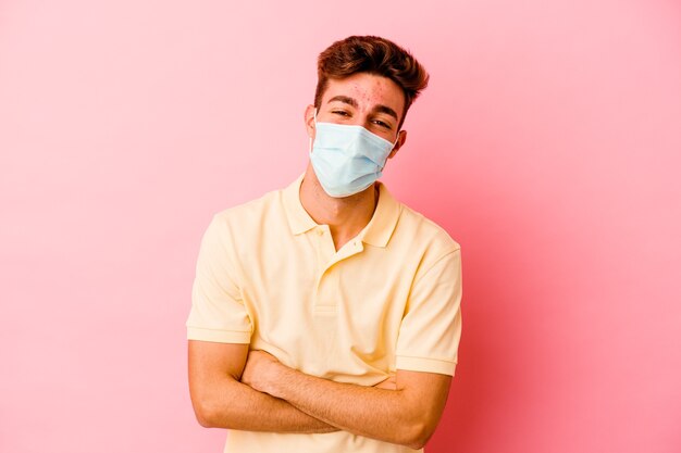 Young caucasian man wearing a protection for coronavirus isolated on pink background laughing and having fun.