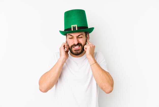 Young caucasian man wearing a saint patricks hat isolated covering ears with hands.