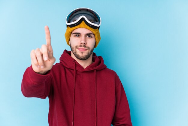 Il giovane uomo caucasico che indossa uno sci copre isolato mostrando il numero uno con il dito.