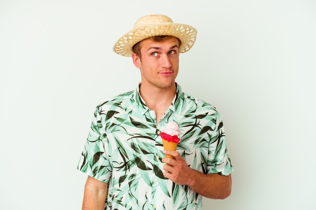 Foto giovane uomo caucasico che indossa abiti estivi e tiene in mano un gelato isolato su bianco sognando di raggiungere obiettivi e scopi