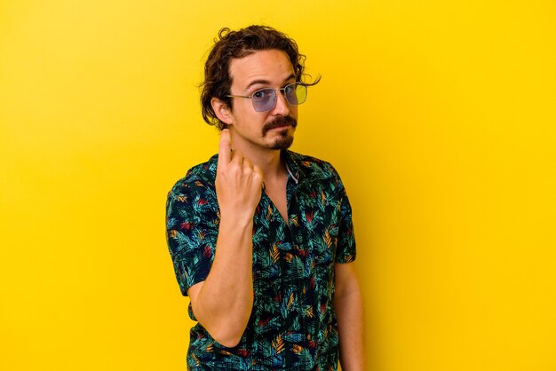 Young caucasian man wearing summer clothes isolated on yellow background pointing with finger at you as if inviting come closer