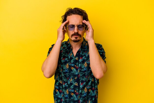 Young caucasian man wearing summer clothes isolated on yellow wall touching temples and having headache