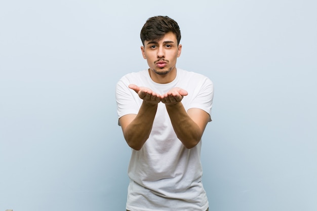 Young caucasian man wearing a white tshirt folding lips and holding palms to send air kiss.