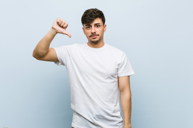 Young caucasian man wearing a white tshirt showing a dislike gesture, thumbs down. Disagreement concept.