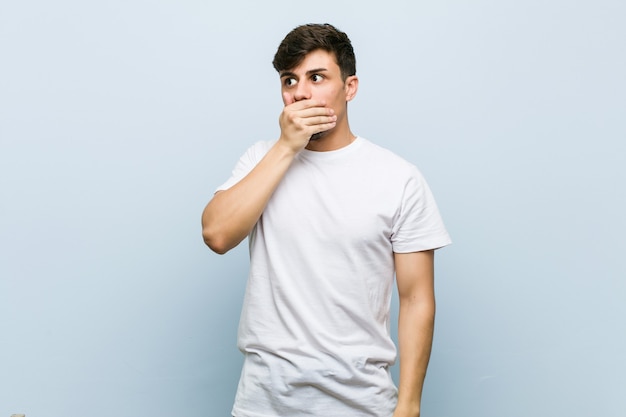 Young caucasian man wearing a white tshirt thoughtful looking to a copy space covering mouth with hand.