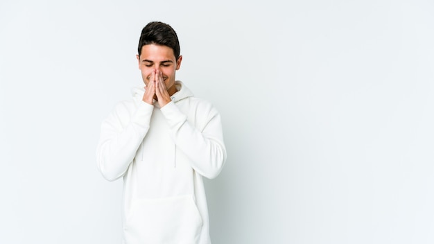 Young caucasian man on white holding hands in pray near mouth, feels confident.