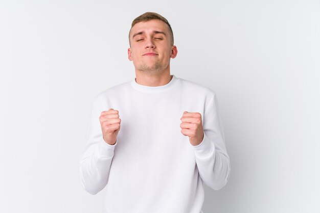 Young caucasian man on white raising fist, feeling happy and successful. Victory concept.