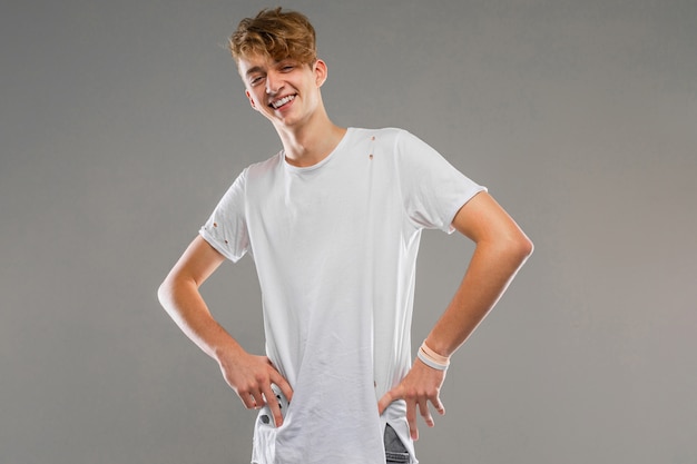 Photo young caucasian man in white t-shirt posing and gesticulating  isolated on grey wall