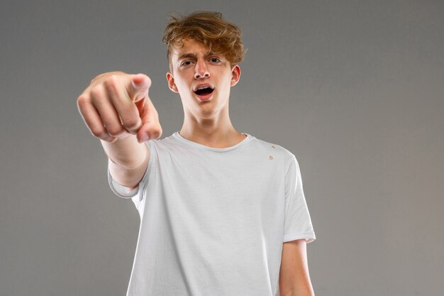 Young caucasian man in white t-shirt posing and gesticulating  isolated on grey wall