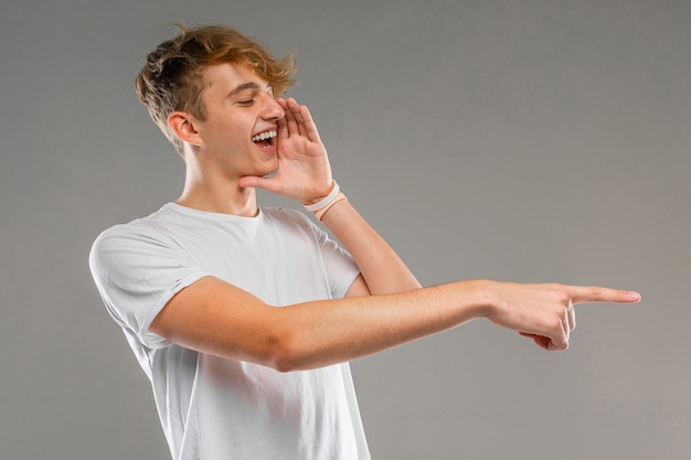 Young caucasian man in white t-shirt posing and gesticulating  isolated on grey wall