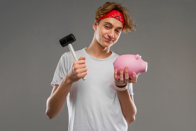 Young caucasian man , white t-shirt with pink pig money box on grey wall