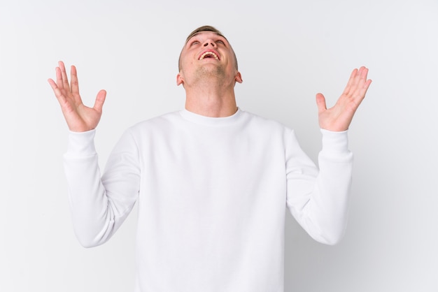 Young caucasian man on white wall screaming to the sky, looking up, frustrated.