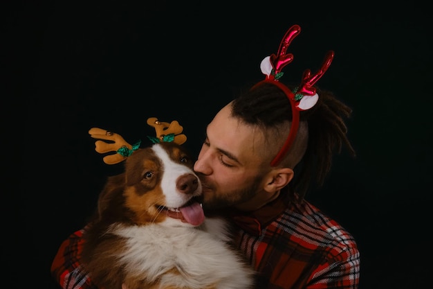 Young Caucasian man with beard and dreadlocks hugs Australian Shepherd and kisses smiling