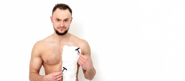 Young caucasian man with beard holds razor shaves his chest with white shaving foam on white surface. Man shaving his torso