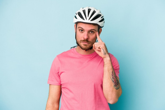 Young caucasian man with bike helmet isolated on blue background pointing temple with finger, thinking, focused on a task.