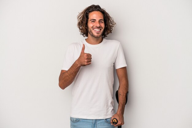 Young caucasian man with crutches isolated on gray background smiling and raising thumb up