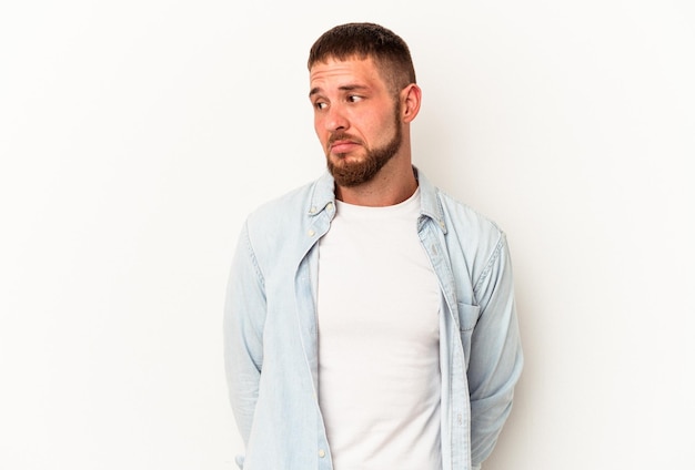 Young caucasian man with diastema isolated on white background shrugs shoulders and open eyes confused.