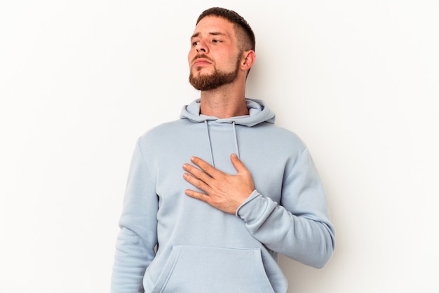 Young caucasian man with diastema isolated on white background taking an oath, putting hand on chest.