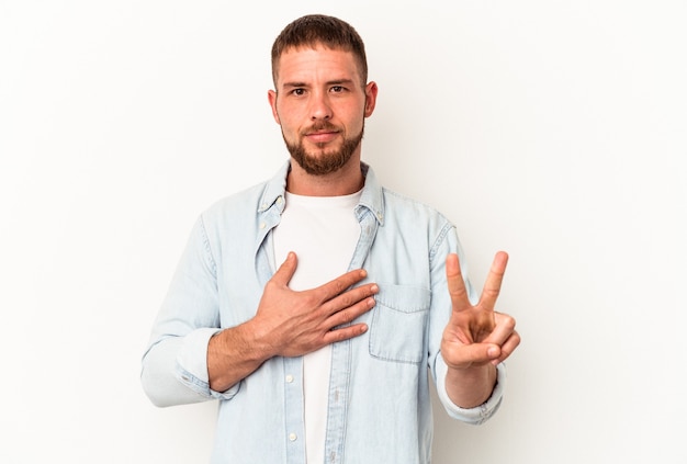 Giovane uomo caucasico con diastema isolato su sfondo bianco prestando giuramento, mettendo la mano sul petto.