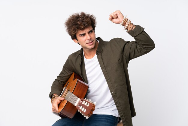 Young caucasian man with guitar over isolated white wall making strong gesture