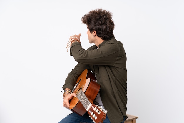 Young caucasian man with guitar pointing back with the index finger