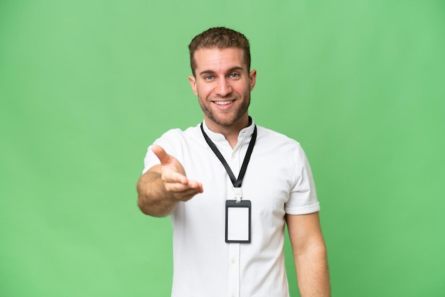 Young caucasian man with ID card isolated on green chroma background shaking hands for closing a good deal