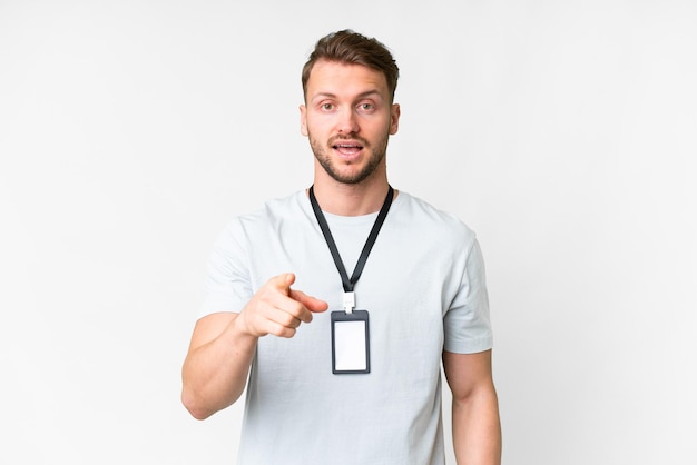 Young caucasian man with ID card over isolated white background surprised and pointing front