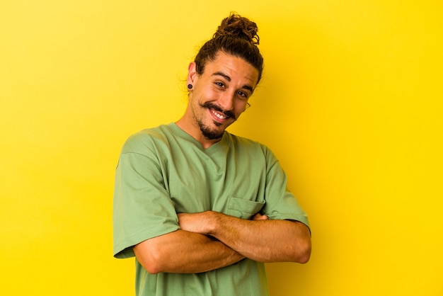 Young caucasian man with long hair isolated on yellow background laughing and having fun.