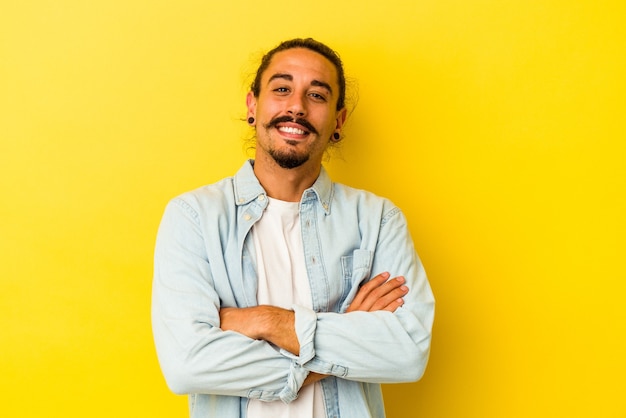 Young caucasian man with long hair isolated on yellow background laughing and having fun.