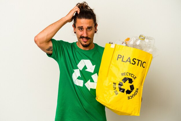 Young caucasian man with long hair recycling plastic isolated on white background being shocked, she has remembered important meeting.