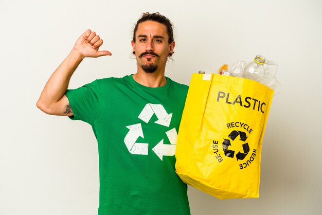 白い背景にプラスチックをリサイクルする長い髪の若い白人男性は、誇りと自信を持って、従うべき例を示しています。