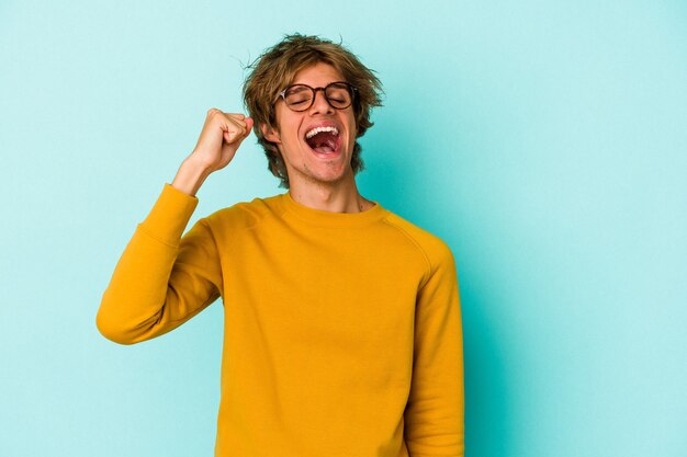 Young caucasian man with make up isolated on blue background  celebrating a victory, passion and enthusiasm, happy expression.