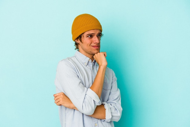 Young caucasian man with make up isolated on blue background  confused, feels doubtful and unsure.