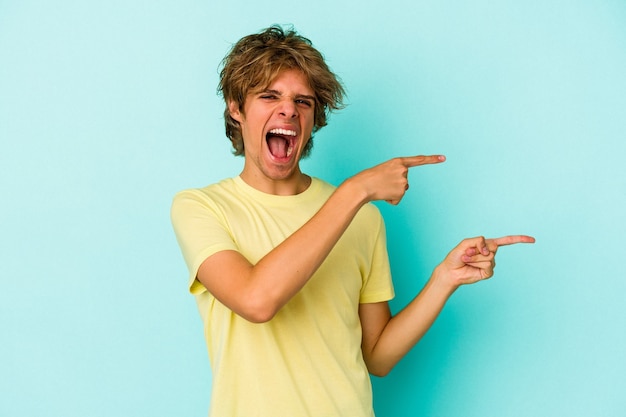 Young caucasian man with make up isolated on blue background  excited pointing with forefingers away.