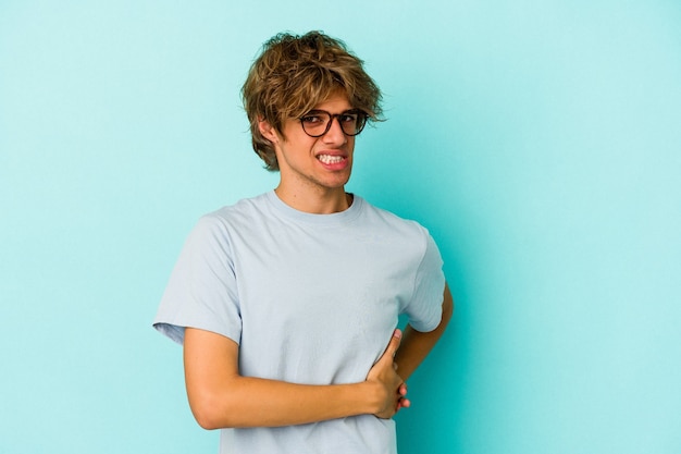 Young caucasian man with make up isolated on blue background  having a liver pain, stomach ache.