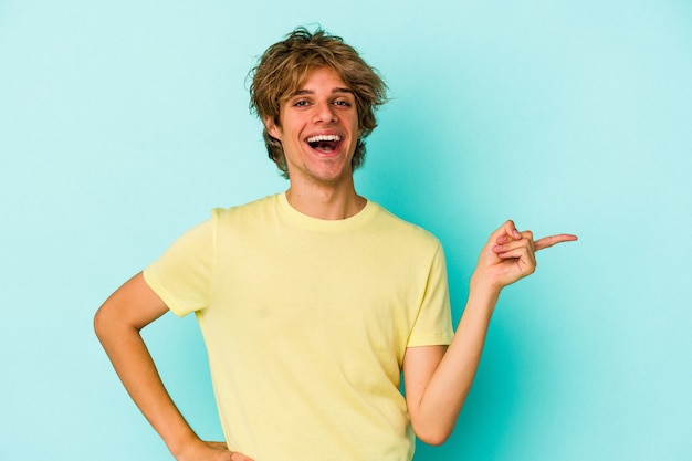 Young caucasian man with make up isolated on blue background  smiling cheerfully pointing with forefinger away.